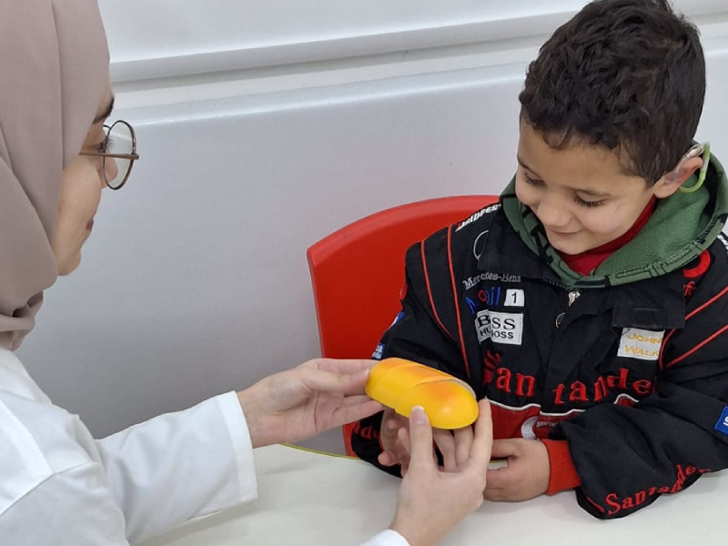 A child looking at a small orange prop being presented to him by a doctor