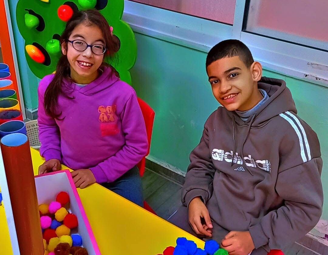Two teenage children smiling for the camera at a yellow table
