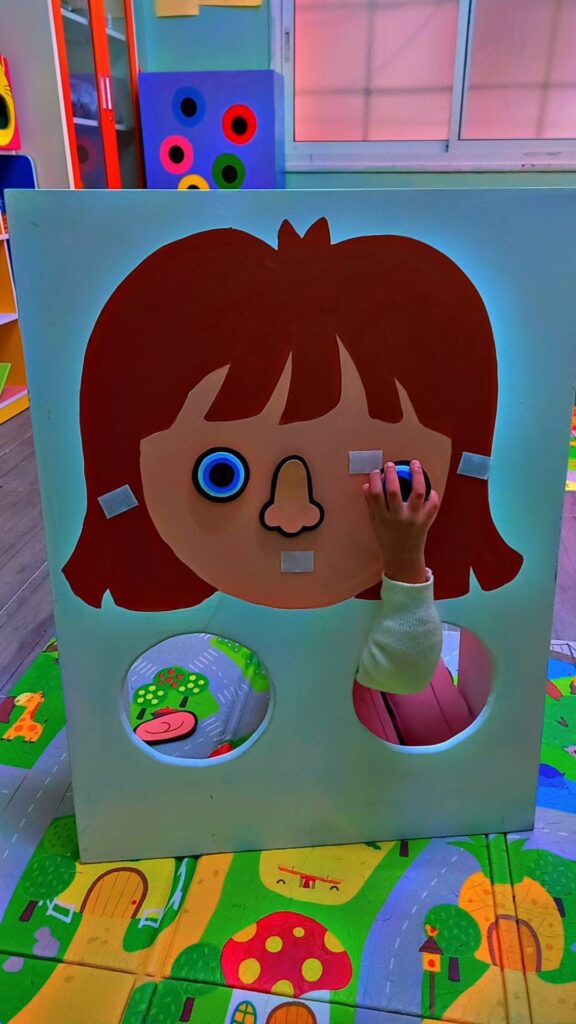 A large painted interactive head with an arm poking through a hole under the head sticking an eye onto a piece of velcro